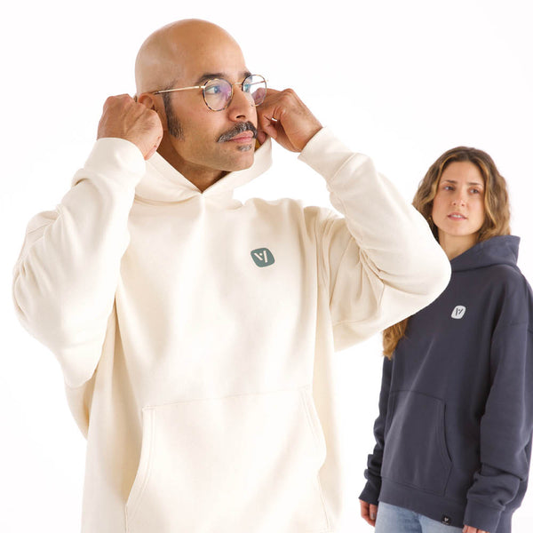 Mann und Frau in veercrew Hoodie "Current", der Mann in Naturweiß mit Kapuze am Kopf, die Frau in Dunkelblau dahinter