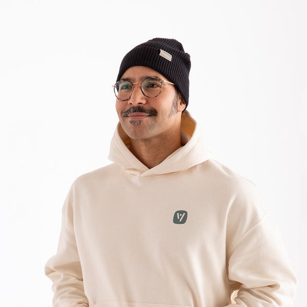 Mann mit schwarzer veercrew Beanie und Brille, in naturweißem Hoodie