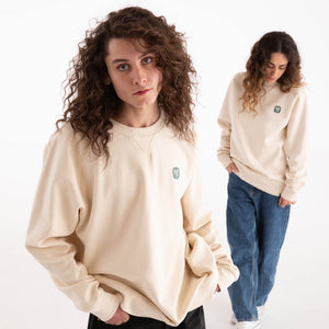 Mann und Frau in naturweißem veercrew Sweatshirt "Pillar" mit kleinem Logo-Print, der Mann vorne, die Frau dahinter