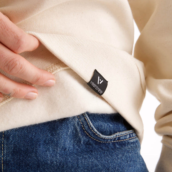 Detailansicht des naturweißen veercrew Sweatshirts "Pillar", Saum leicht angehoben mit Blick auf das Innenfutter und das eingenähte veercrew Label
