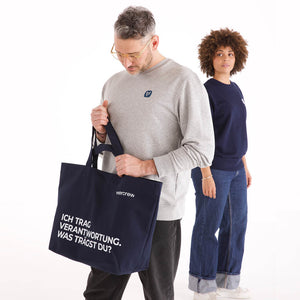 Dunkelblaue veercrew Tragetasche "Vessel" mit Aufschrift "Ich trag Verantwortung. Was trägst du?", getragen von einem Mann im grauen Sweatshirt